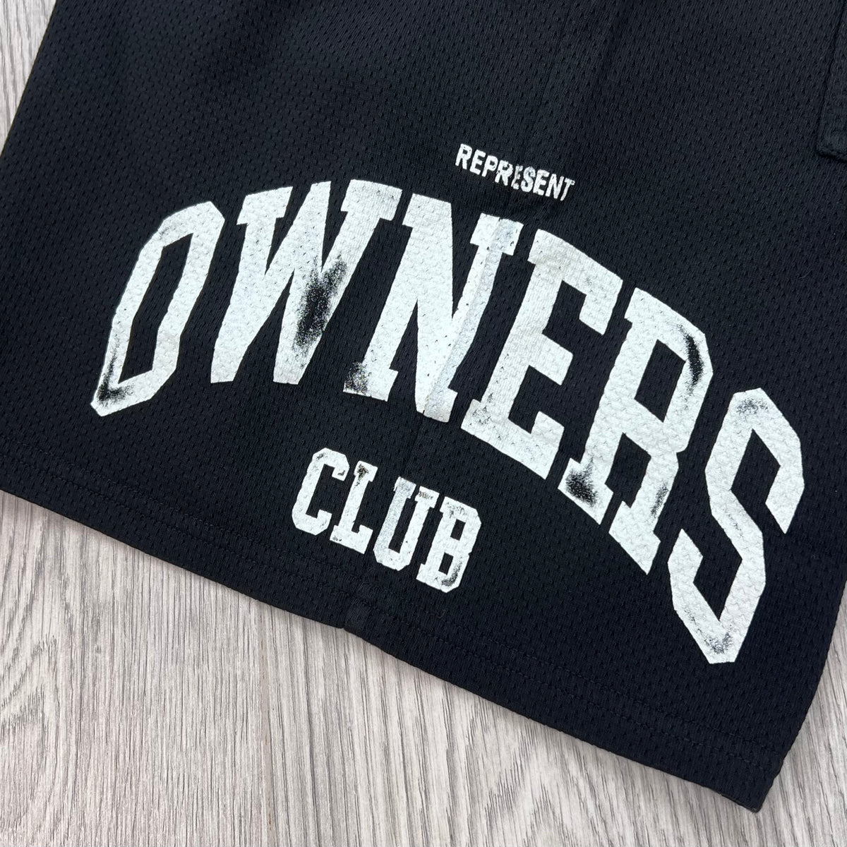 A close up view of the screen printed logo on the Represent Owners Club Mesh Shorts in Black.